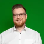 Foto von Klemens Viehmann, einem Mann mit heller Haut, kurzen braunen Haaren und einem kurzen rotbraunen Bart. Er trägt eine dunkle eckige Brille und ein weißes Hemd und blickt lächelnd in die Kamera.